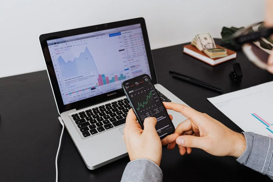 Hands typing on a laptop with cryptocurrency charts and smartphone display in view, focusing on digital finance.